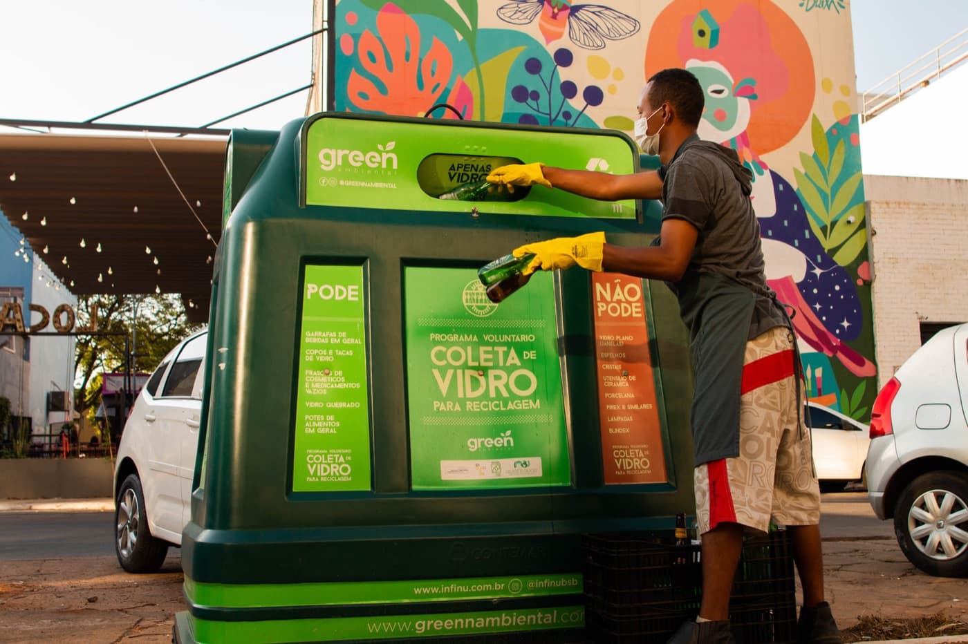 An Ecozinha worker placing a glass bottle into a green collection container.