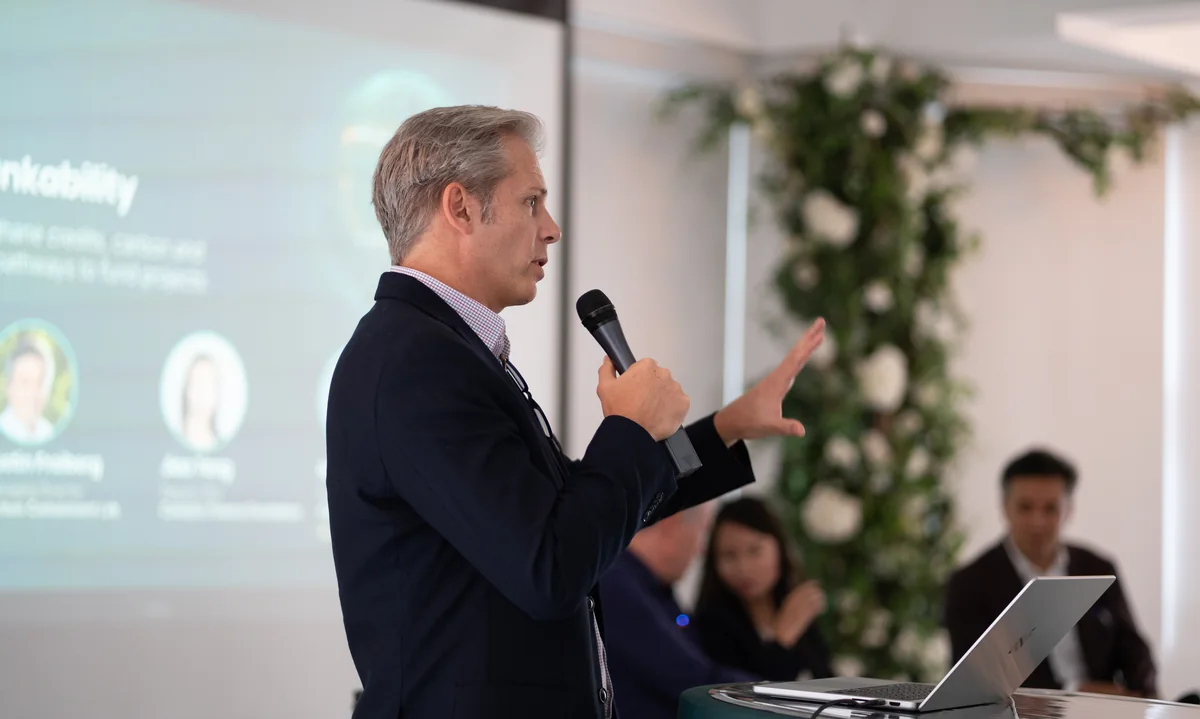 Ian McKee speaking into a microphone at Bryant Park Loft, the Methane Bankability slide behind him